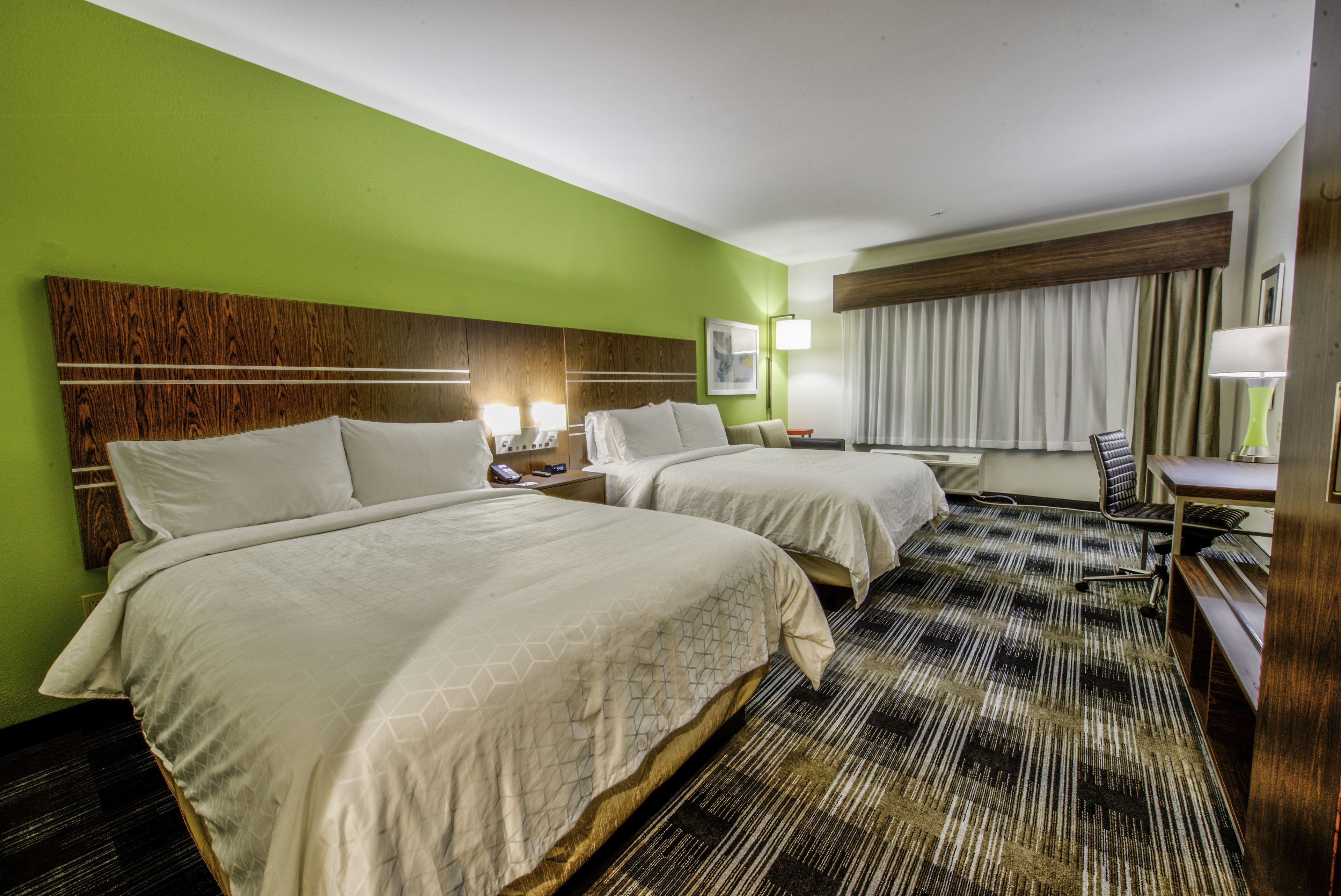 A hotel room with two beds, a desk, a chair, and a large window with curtains.