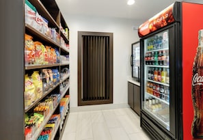 A snack aisle with various chips and snacks, a beverage refrigerator stocked with sodas, and a Coca-Cola vending machine. - Holiday Inn Express & Suites Dallas NW - Farmers Branch by IHG (Farmers Branch)