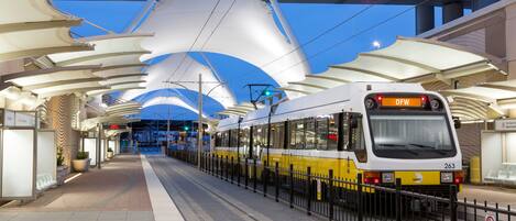 A tram at a station with a modern architectural design, including a curved roof structure and a digital display showing the time.