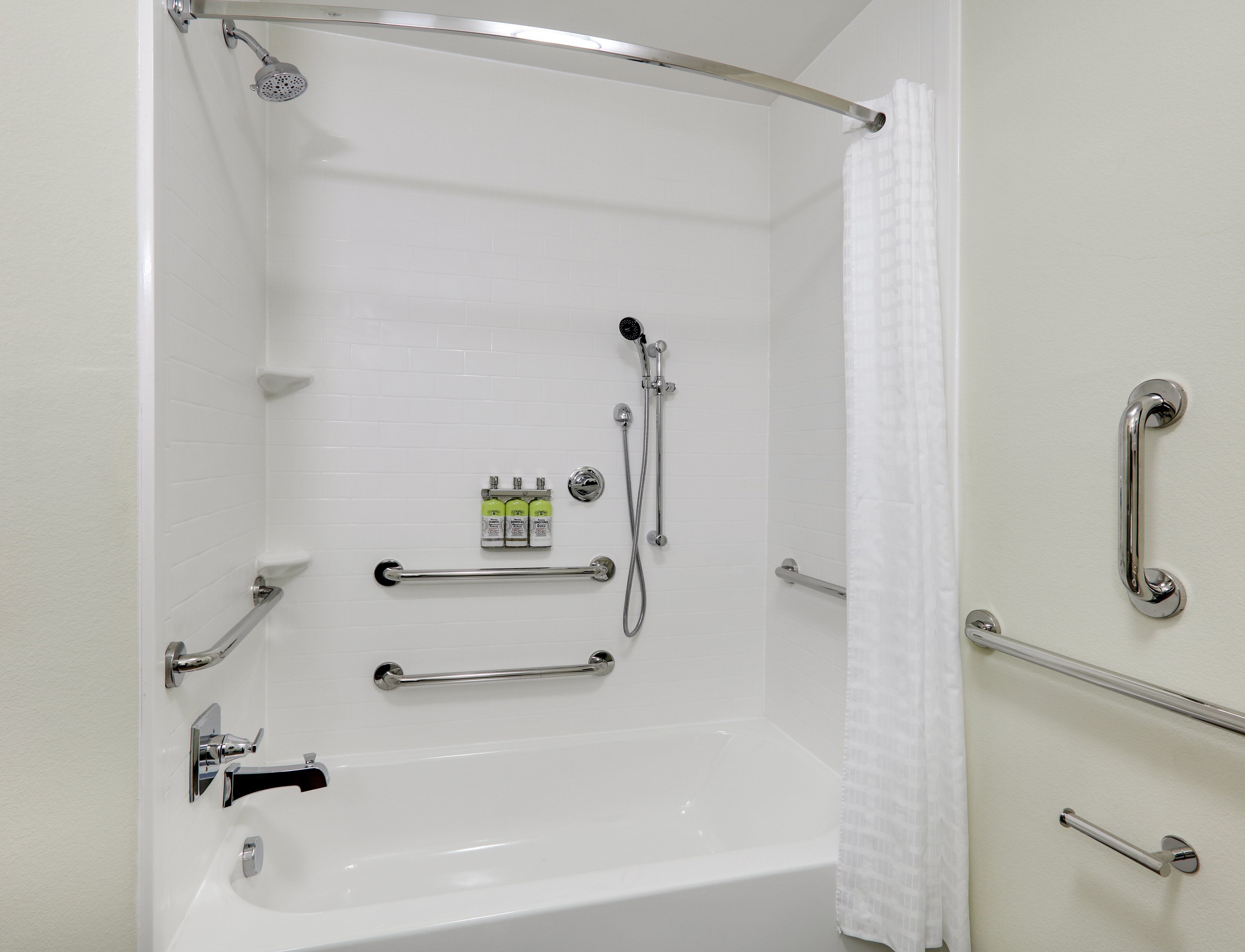 Une salle de bain moderne équipée d’une baignoire, de barres d’appui, d’un pommeau de douche et d’un porte-serviettes.