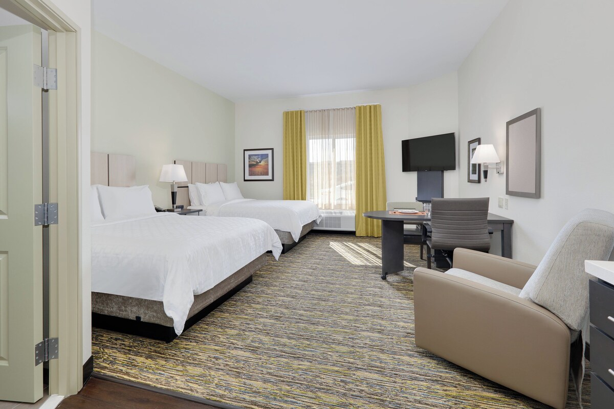 Quarto de hotel com duas camas, uma escrivaninha, uma cadeira, uma televisão e uma janela com cortinas.