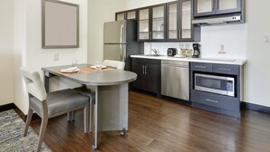 A modern kitchen with stainless steel appliances, a dining area with a round table and chairs, and a built-in oven. - Candlewood Suites Dallas NW - Farmers Branch by IHG (Farmers Branch)