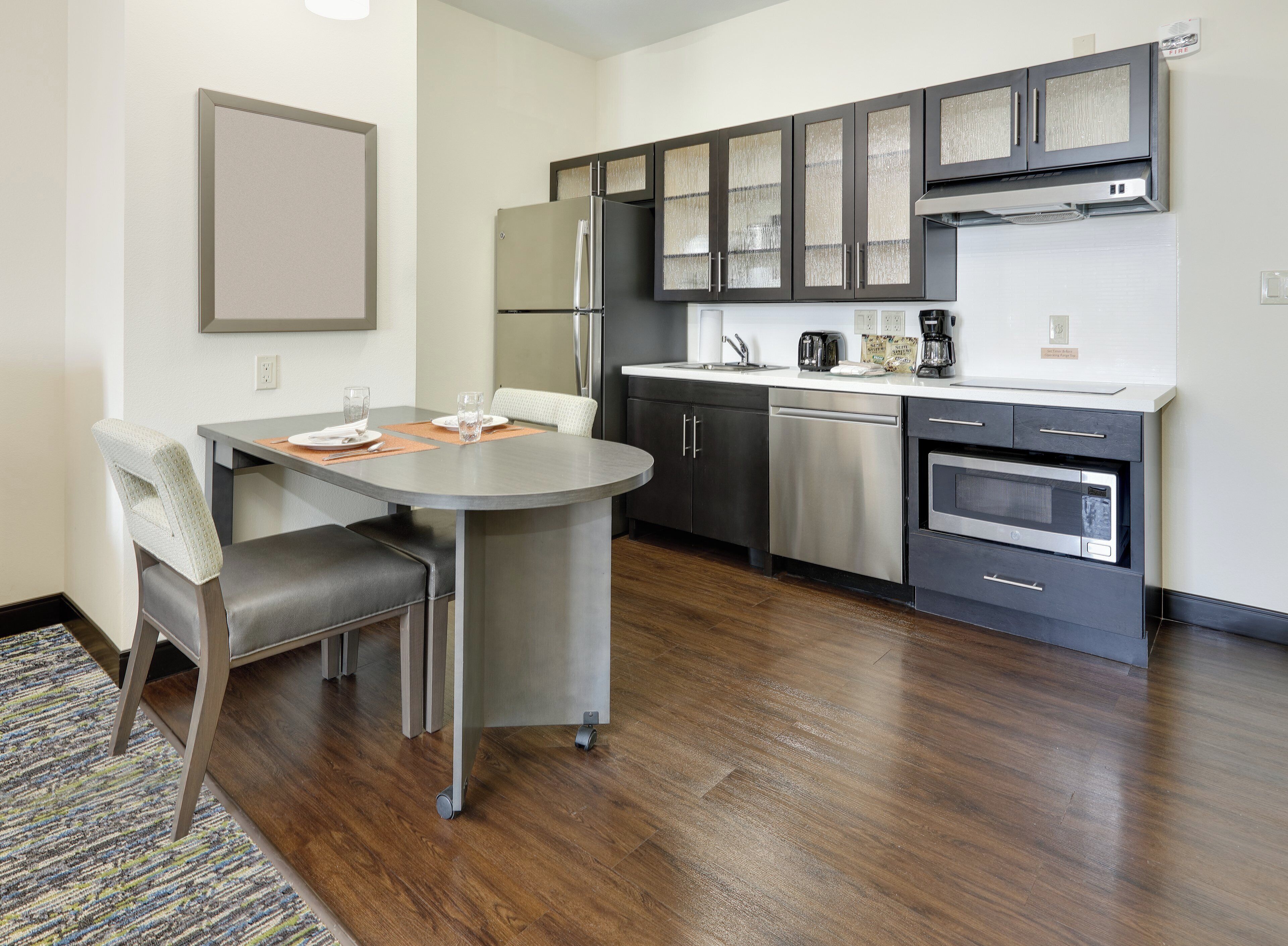 A modern kitchen with stainless steel appliances, a dining area with a table and chairs, and a patterned rug on the floor.