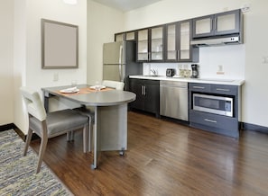 A modern kitchen with stainless steel appliances, a dining area with a table and chairs, and a patterned rug on the floor. - Candlewood Suites Dallas NW - Farmers Branch by IHG (Farmers Branch)