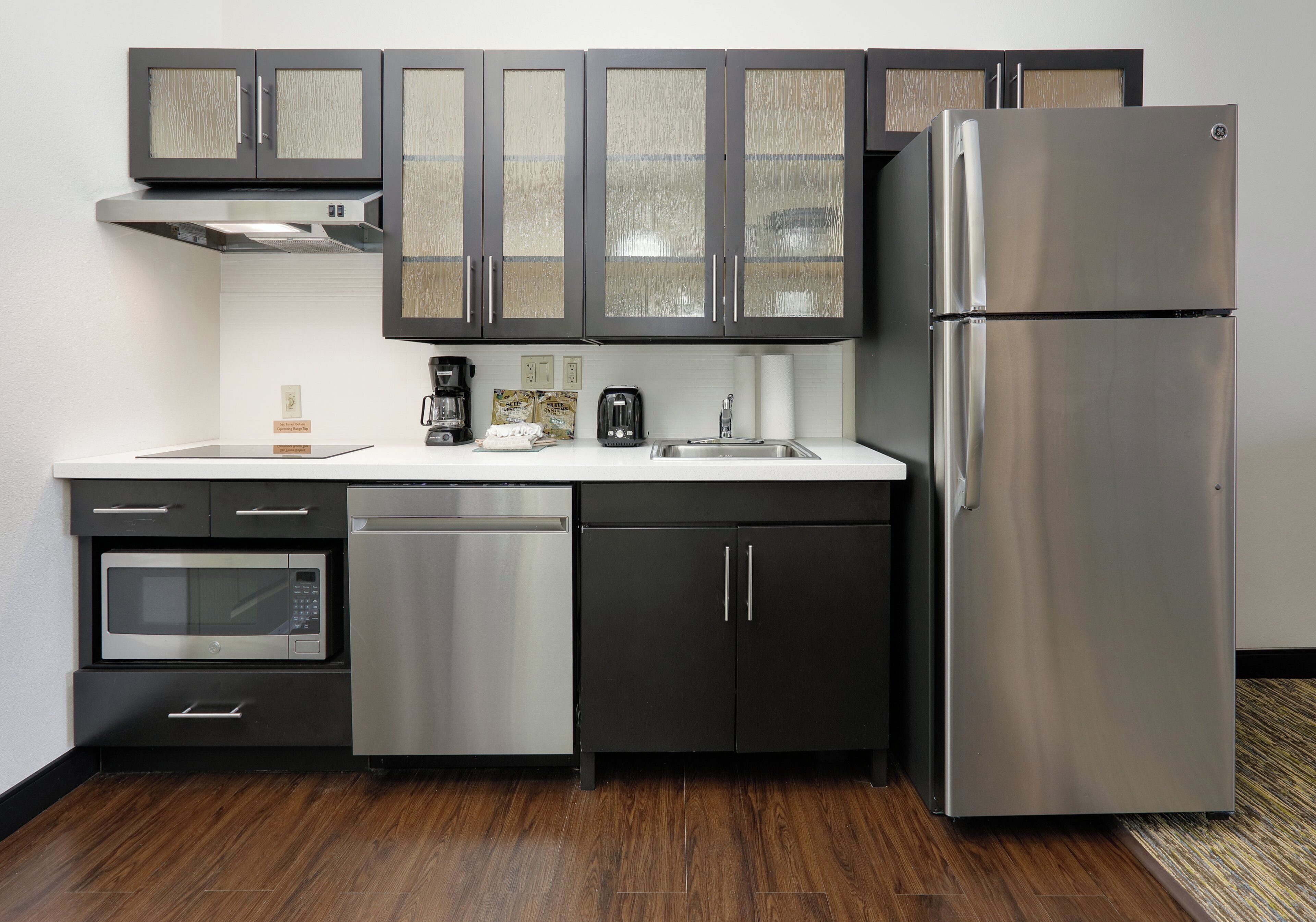 A modern kitchen with stainless steel appliances, including a refrigerator, oven, and dishwasher, and dark cabinetry with glass doors.