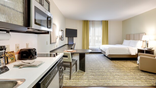A hotel room with a kitchenette, a dining area, and a bed. - Candlewood Suites Dallas NW - Farmers Branch by IHG (Farmers Branch)