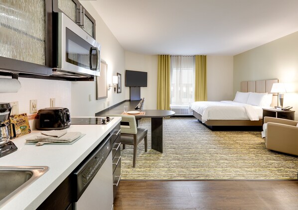 Quarto de hotel com cozinha compacta, espaço para refeições e uma cama.