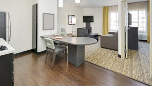 A modern hotel room with a dining area, a sofa, a flat-screen TV, and a minibar. - Candlewood Suites Dallas NW - Farmers Branch by IHG (Farmers Branch)