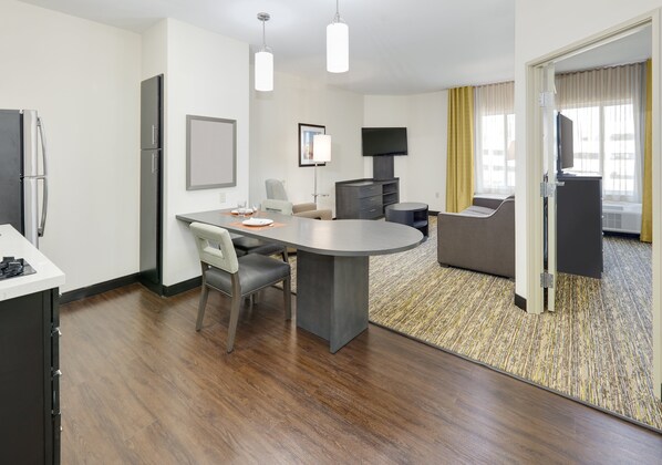A modern hotel room with a dining area, a sofa, a flat-screen TV, and a minibar. - Candlewood Suites Dallas NW - Farmers Branch by IHG (Farmers Branch)