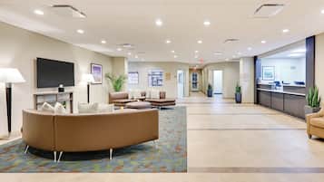 A spacious lobby with a curved sofa, a flat-screen TV, and a reception desk.