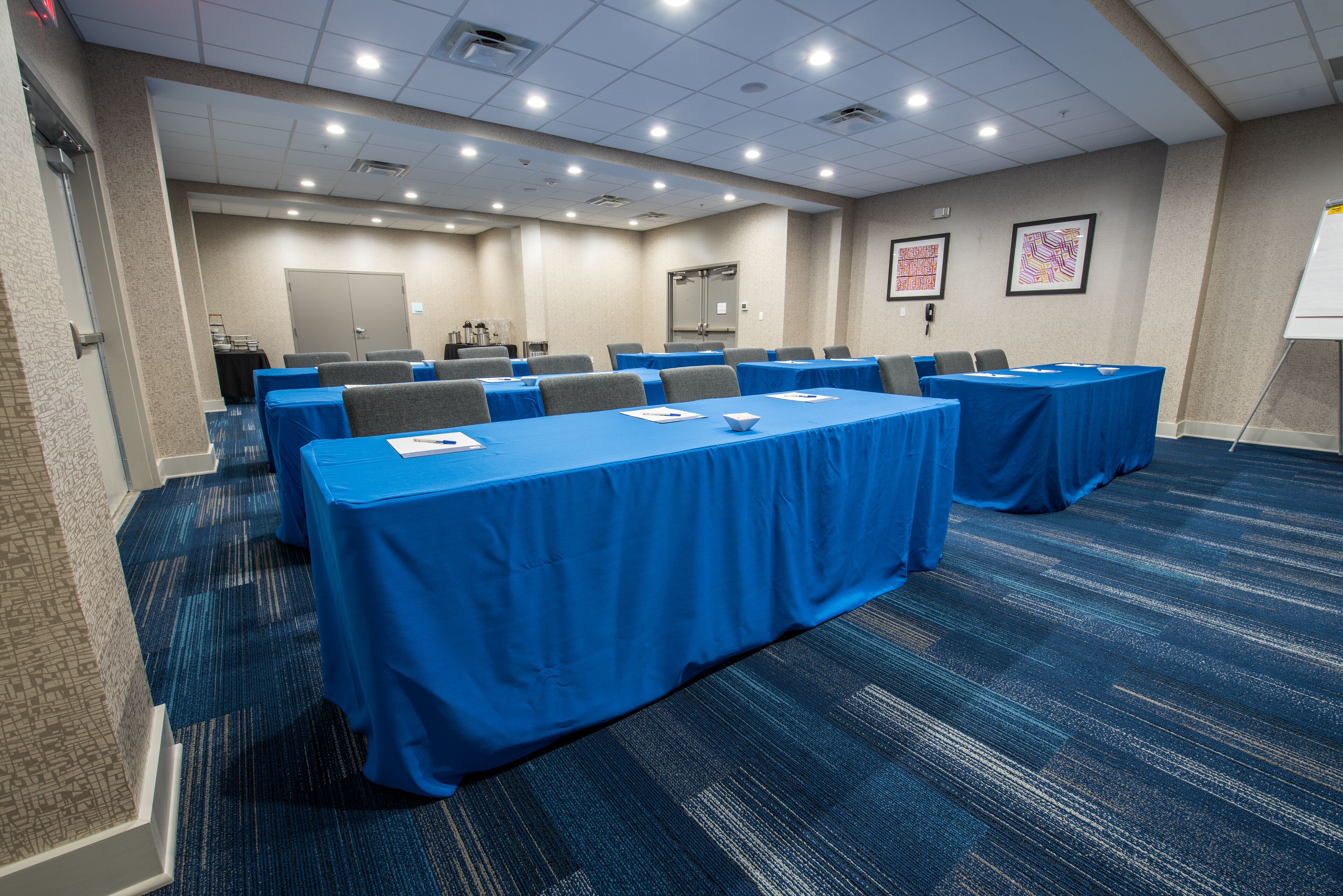 A conference room with multiple tables covered in blue tablecloths, arranged in rows.