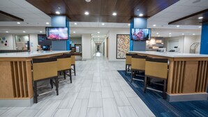 Um hall de hotel moderno com um balcão de recepção central, duas áreas de bar e um longo corredor que se estende até o fundo.