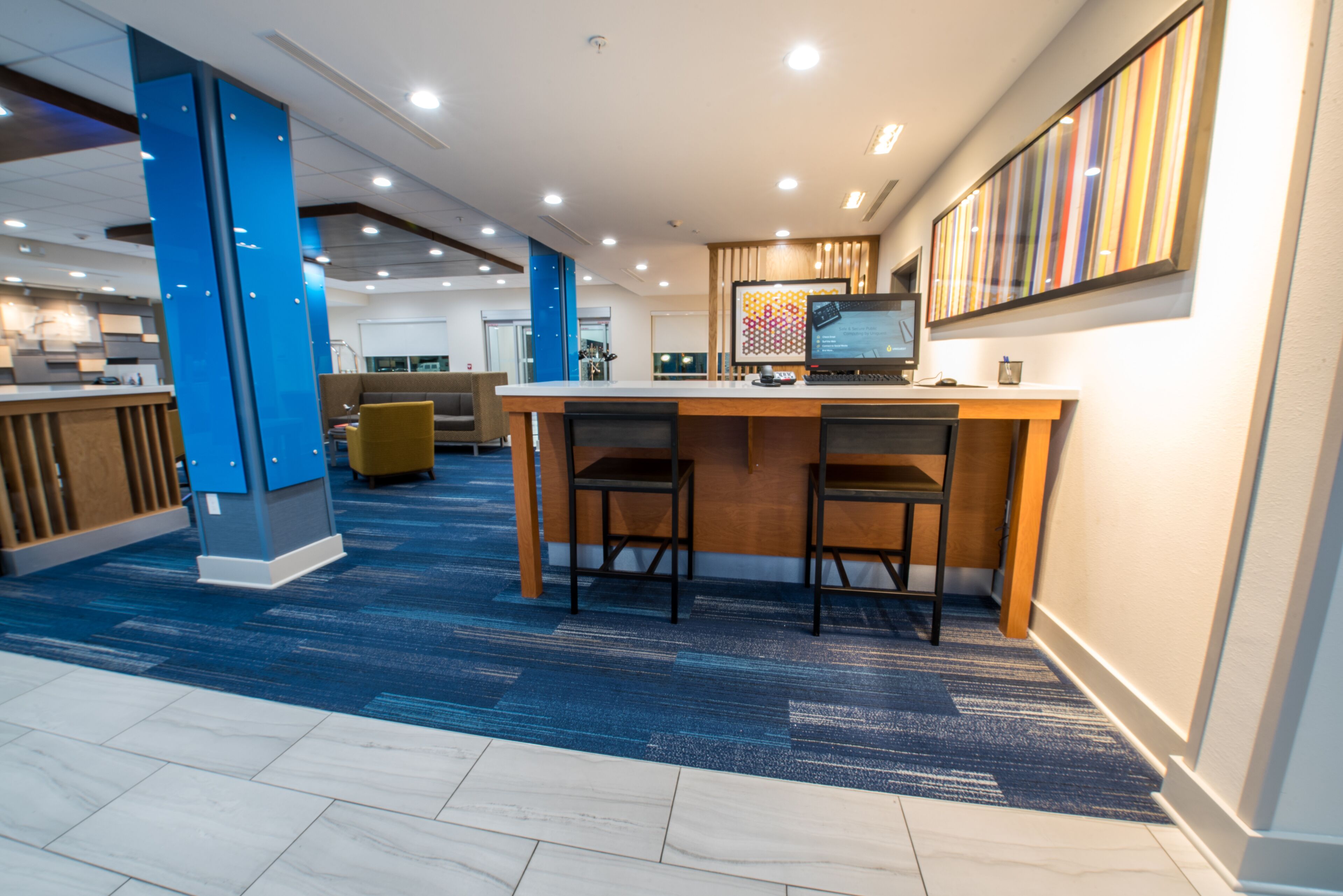 A modern office space with a reception area, a counter, two bar stools, and a large screen on a desk.