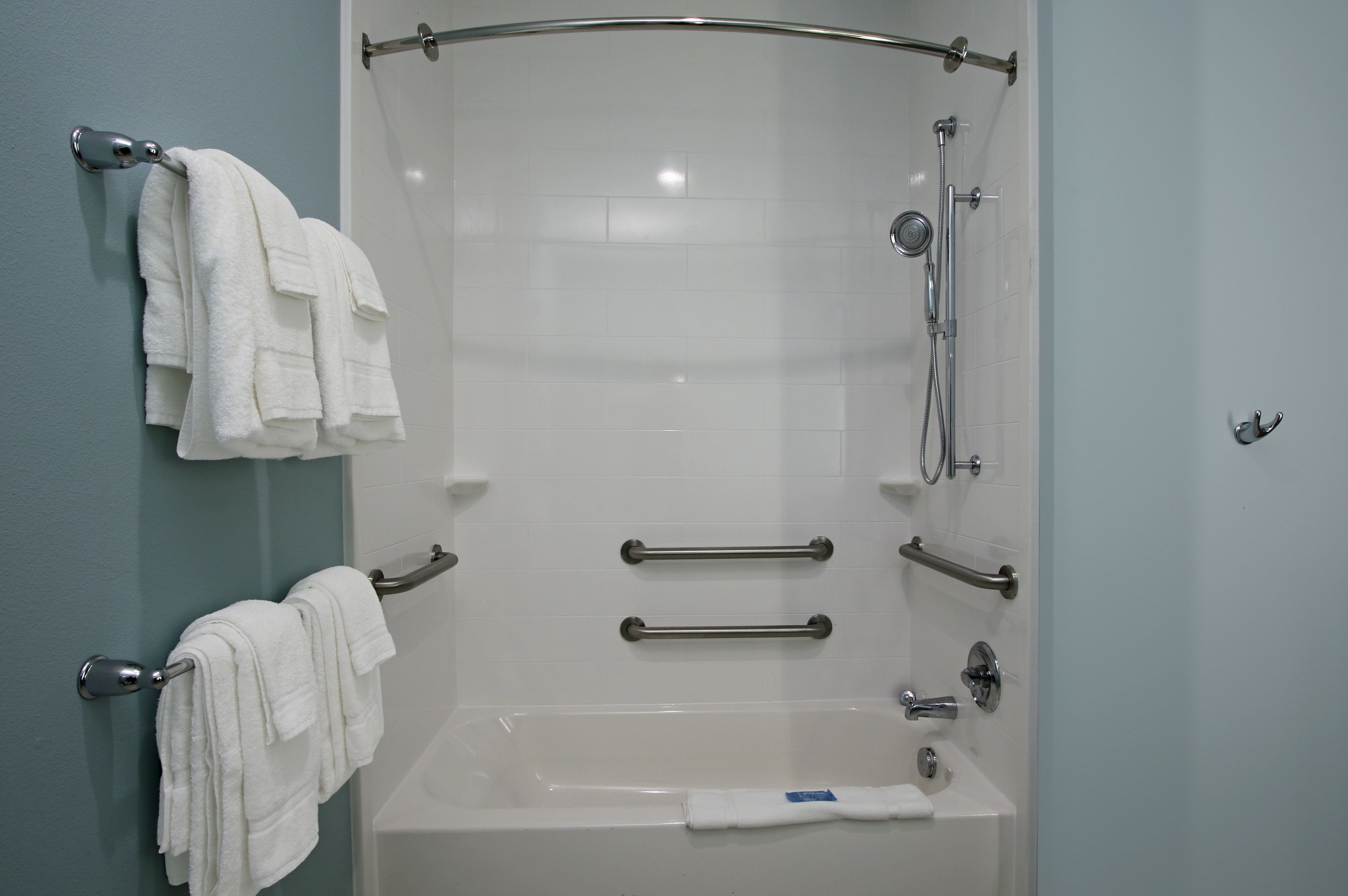 A modern bathroom with a bathtub, grab bars, and a towel rack.