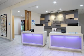 A hotel reception area with two reception desks, a vending machine, and a wall-mounted security camera. - Holiday Inn Express & Suites Lake Charles South Casino Area by IHG (Lake Charles)