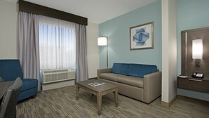 Quarto de hotel com sofá, poltrona, mesa de centro e luminária.