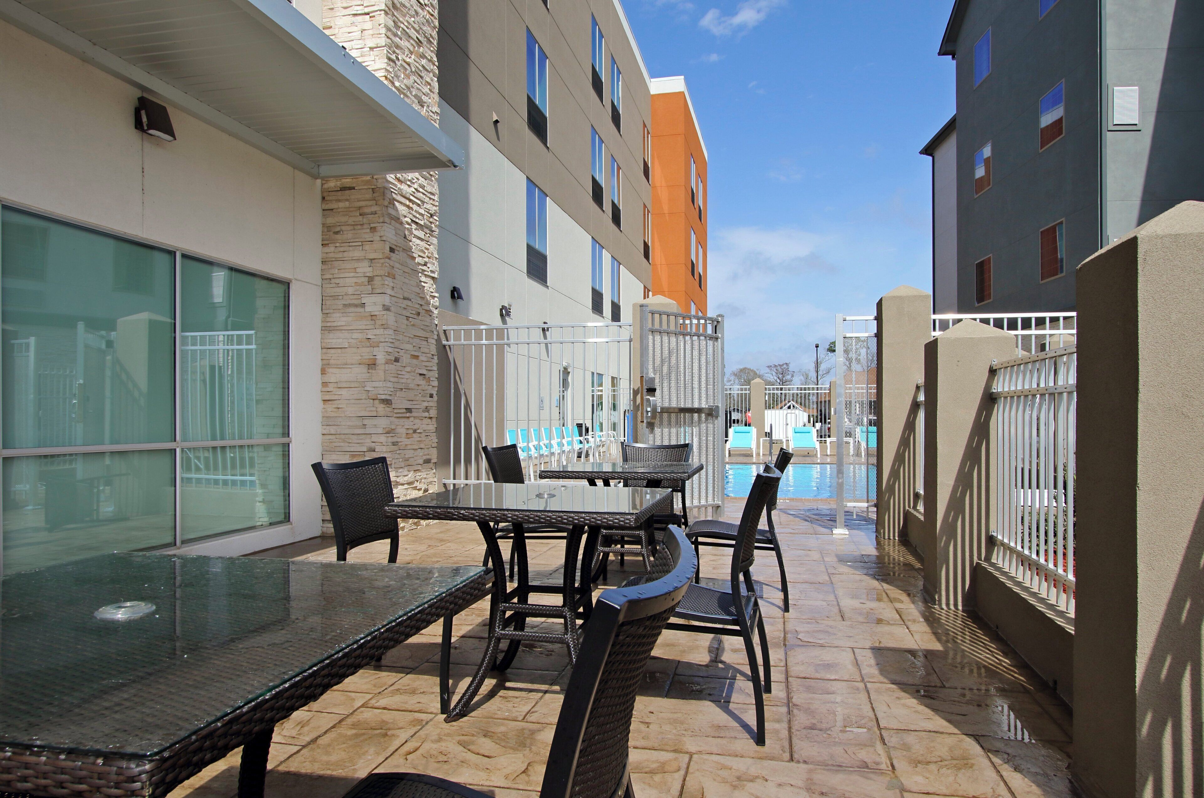 Área da piscina com mesa e cadeiras de vidro, piscina e um edifício com várias janelas e varandas.