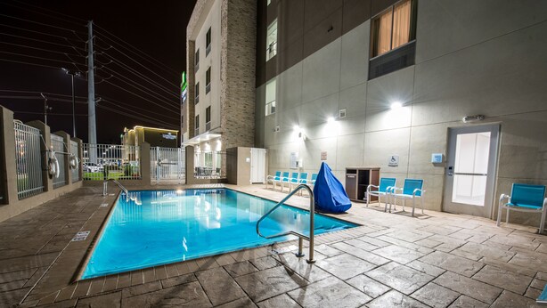 Piscina interna com piso de azulejos, escada de metal e cadeiras azuis ao redor da área da piscina.