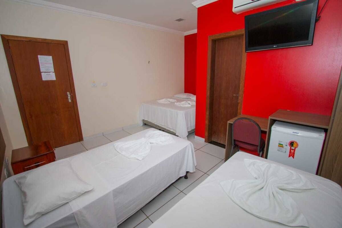 A room with two single beds, a TV mounted on the wall, a small refrigerator, and a wooden door.