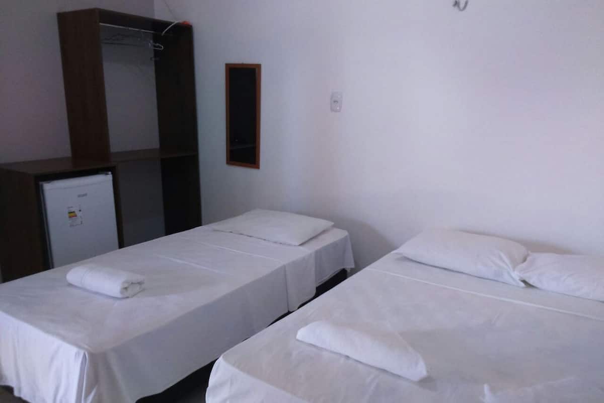 Two single beds with white linens, a wooden wardrobe, and a small refrigerator in a room.