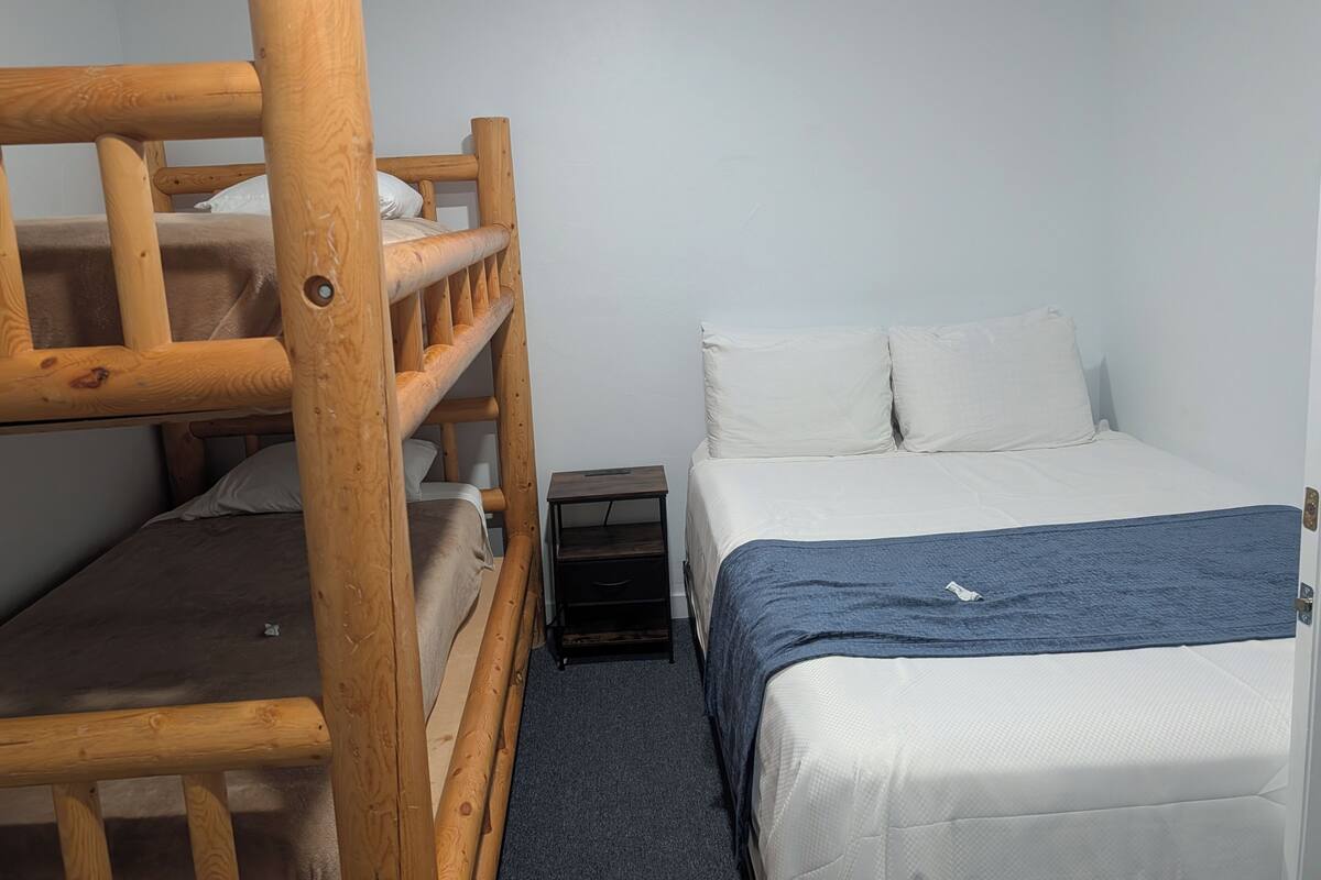 A bunk bed with a wooden frame, a single bed with white bedding, and a small bedside table.
