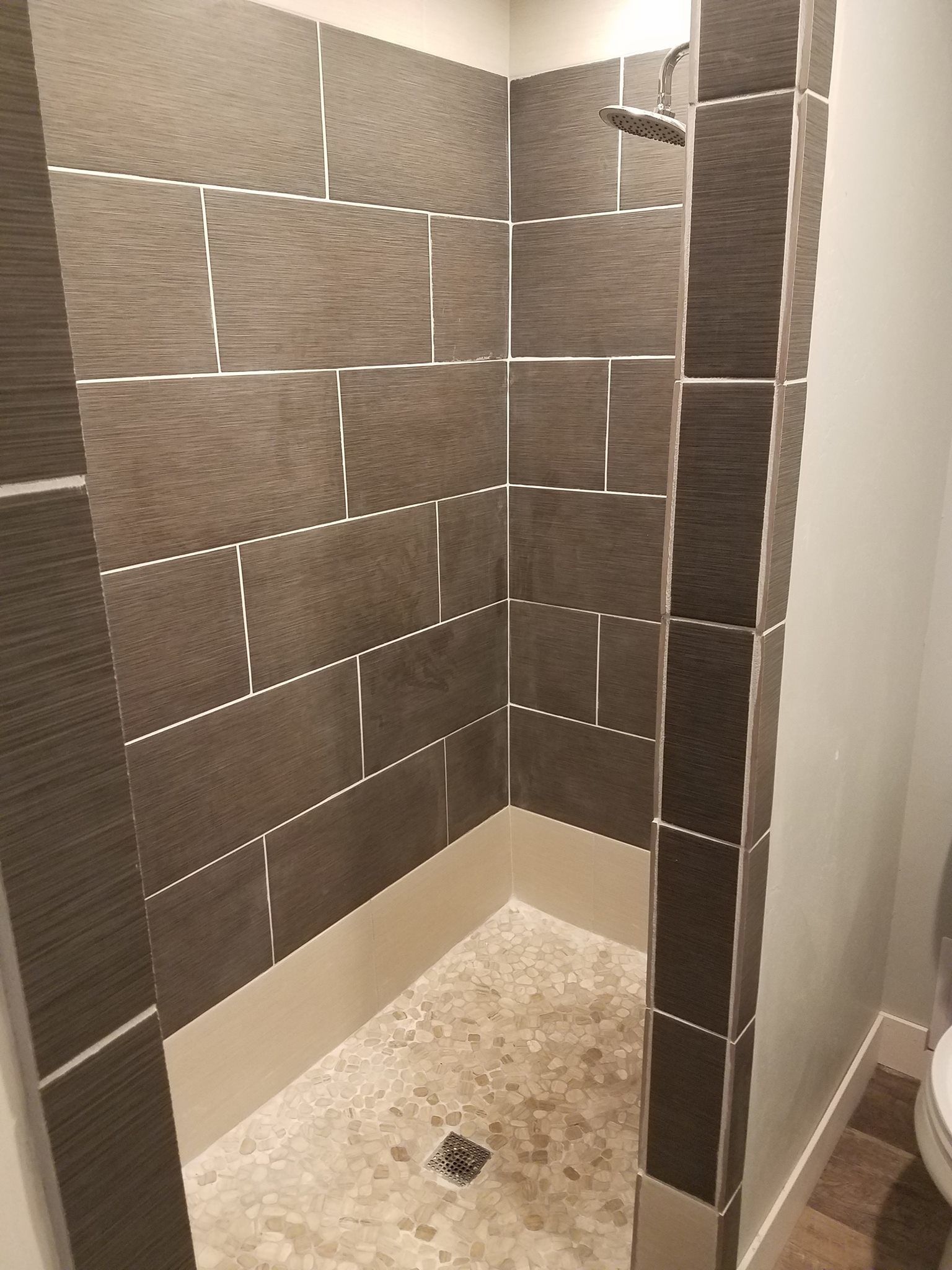 Ducha con azulejos oscuros y un desagüe pequeño.