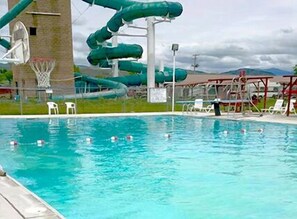 Una piscina con tobogán de agua y aro de baloncesto.