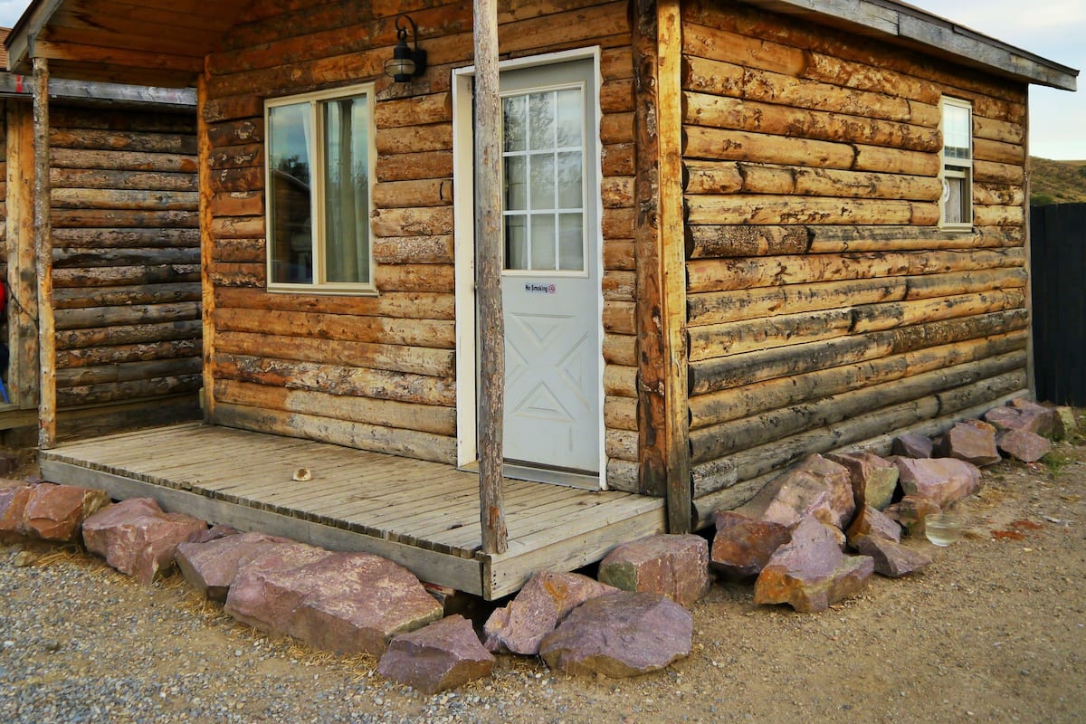 A log cabin with a wooden porch, two windows, and a door.