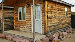 A log cabin with a wooden porch, two windows, and a door.