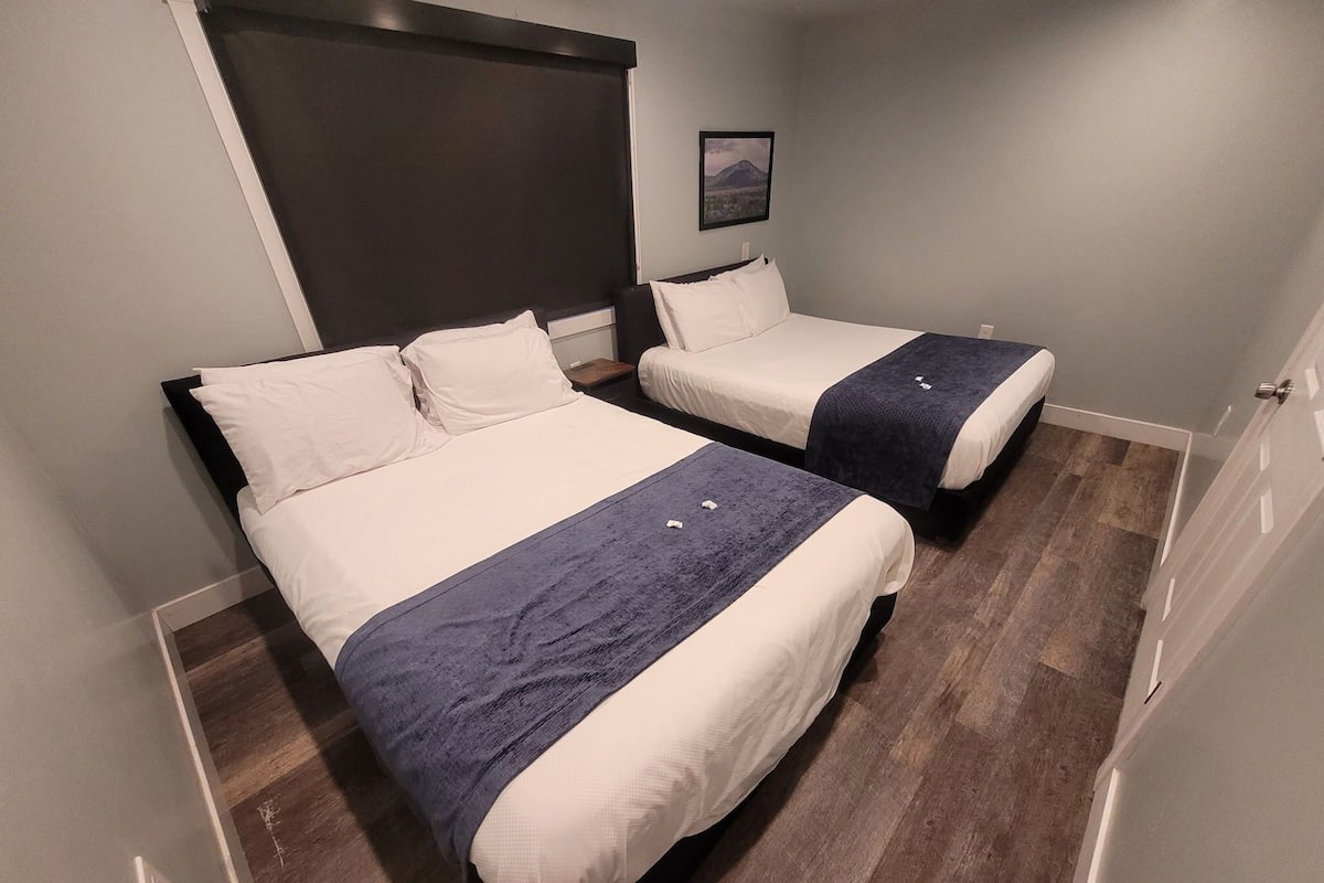 A hotel room with two beds, a dark headboard, a framed picture on the wall, and a wooden floor.