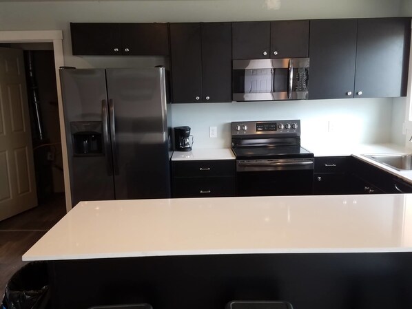 Una cocina moderna con armarios negros, electrodomésticos de acero inoxidable y encimera blanca.