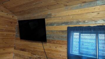 A room with wooden walls, a flat-screen TV mounted on the wall, and a window with blue curtains.