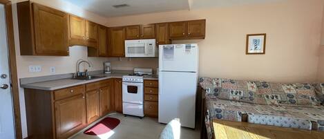 A compact kitchen with wooden cabinets, a microwave, a refrigerator, a stove, and a dining area with a table and chairs.