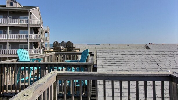 A wooden deck with blue Adirondack chairs, a wooden railing, and a building with multiple balconies and windows.