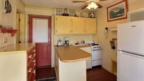 A compact kitchen with wooden cabinets, a white refrigerator, a stove, and a ceiling fan.