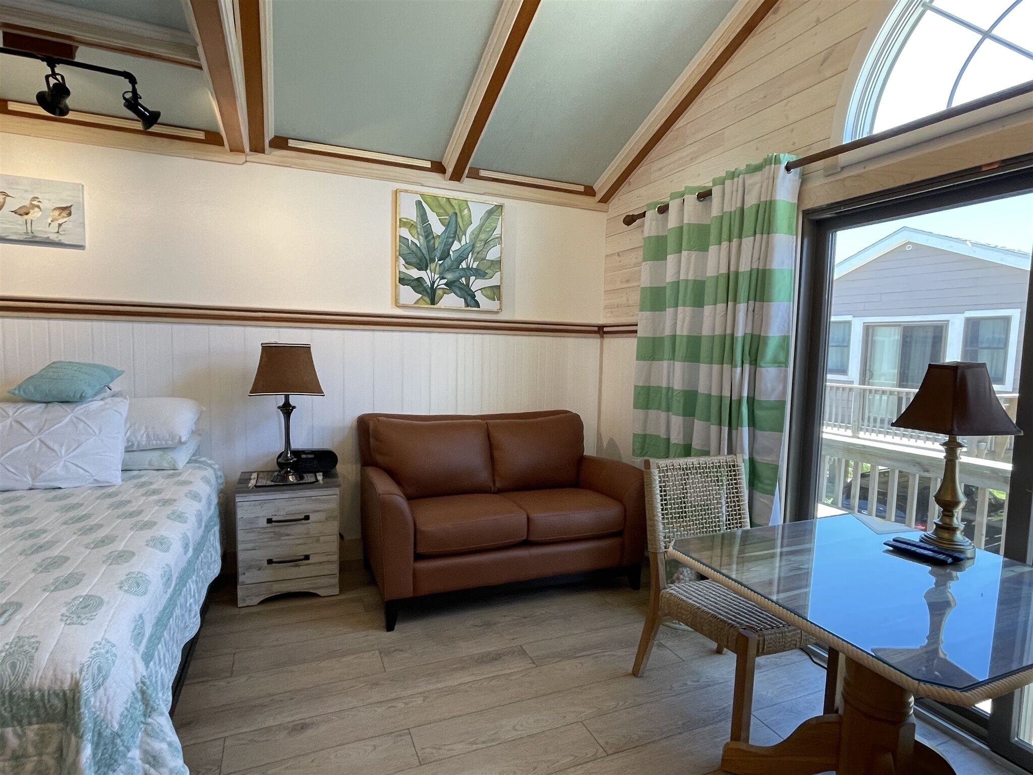A bedroom with a bed, a brown sofa, a glass table, and a window with curtains.