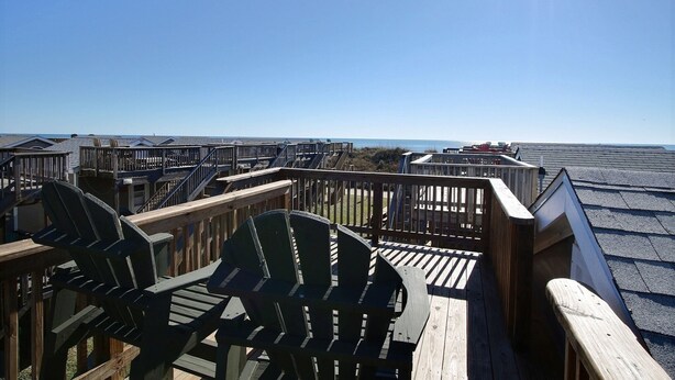 A wooden deck with Adirondack chairs overlooking a beach.