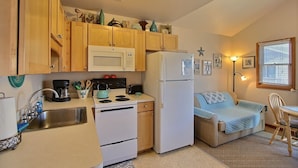 A compact kitchen with wooden cabinets, a microwave, a refrigerator, and a small dining area with a chair and table.