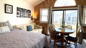 A cozy room with a bed, a round table with chairs, a window with curtains, and framed pictures on the wall.