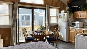 A cozy room with a bed, a dining table with chairs, a kitchen area with a refrigerator, microwave, and cabinets, and a large window with curtains.