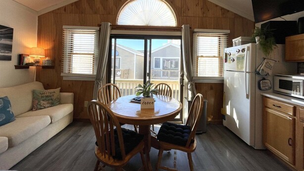 A cozy kitchen with wooden walls, a dining table, chairs, a refrigerator, and a microwave.