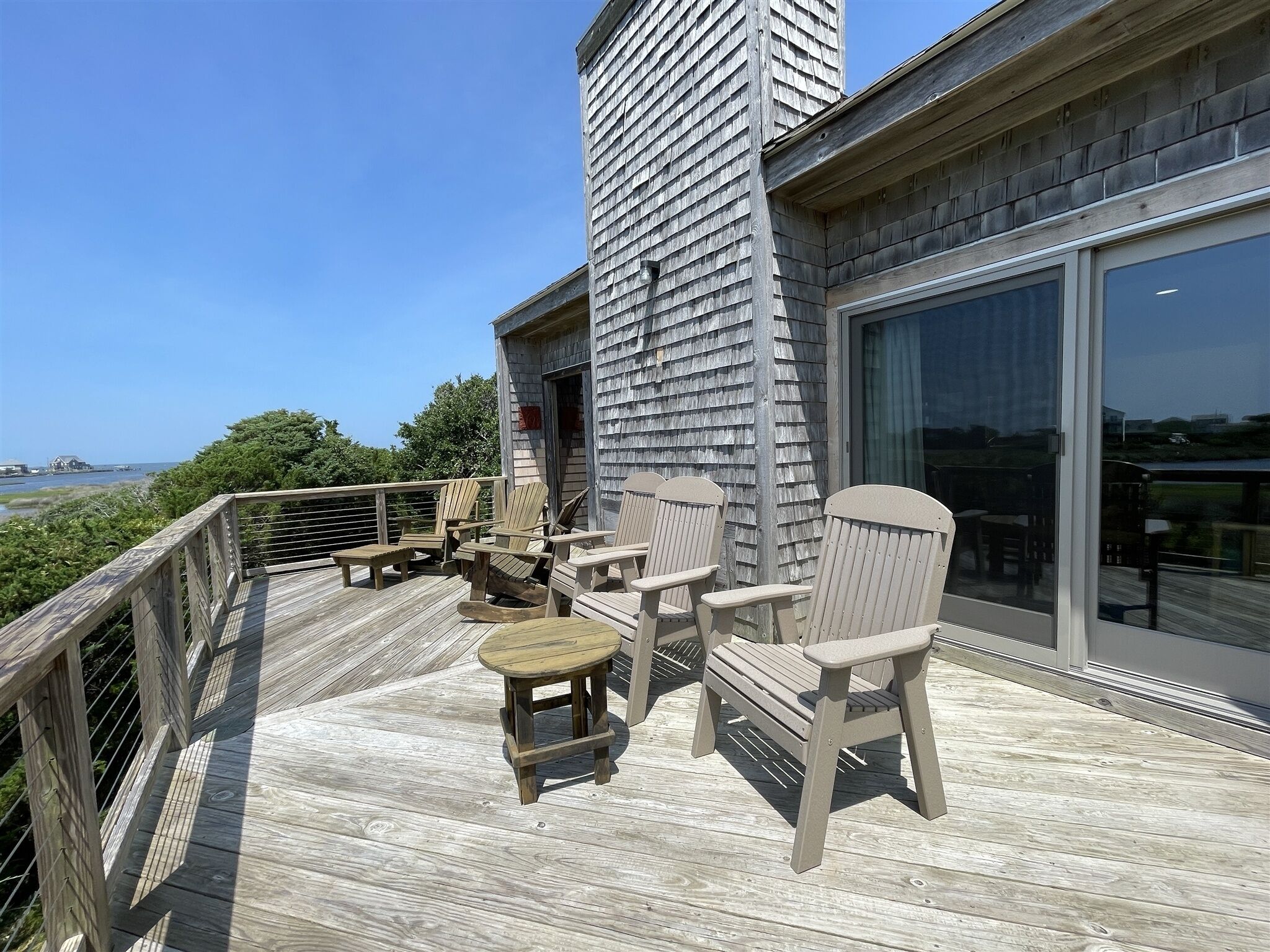 Een houten terras met Adirondack-stoelen en een kleine tafel, met uitzicht op water en groen.