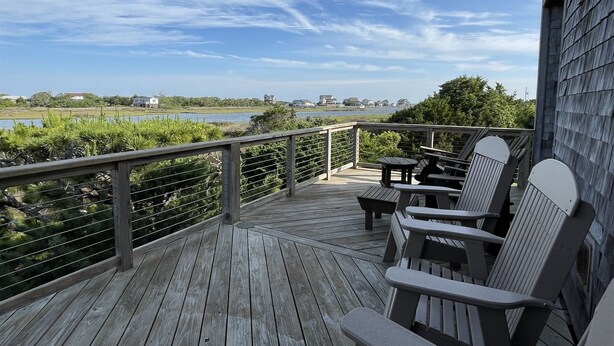 Een houten terras met Adirondack-stoelen met uitzicht op een waterpartij en gebouwen in de verte.