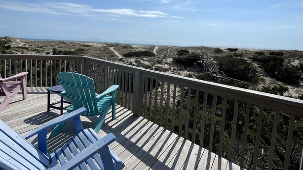 Een houten terras met stoelen en uitzicht op het strand.