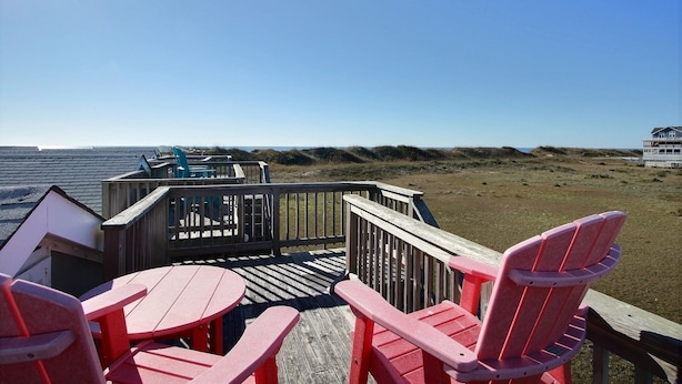 A wooden deck with red Adirondack chairs and a view of the beach. - 4 Carolina Lady Studio Bedroom Condo by RedAwning (Hatteras)