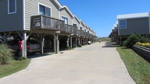 A row of two-story houses with wooden balconies, a concrete driveway, and a clear blue sky. - 34 Sailing In A Gale Studio Bedroom Condo by RedAwning (Hatteras)