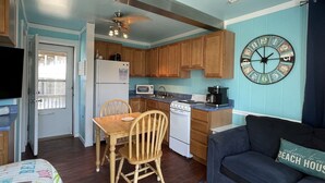 A compact kitchen with wooden cabinets, a refrigerator, microwave, stove, and a ceiling fan. - 34 Sailing In A Gale Studio Bedroom Condo by RedAwning (Hatteras)
