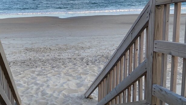 A wooden boardwalk leading to a beach with a clear view of the ocean.