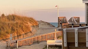 A beach view with a wooden boardwalk, a flag, and a building with a sloped roof.