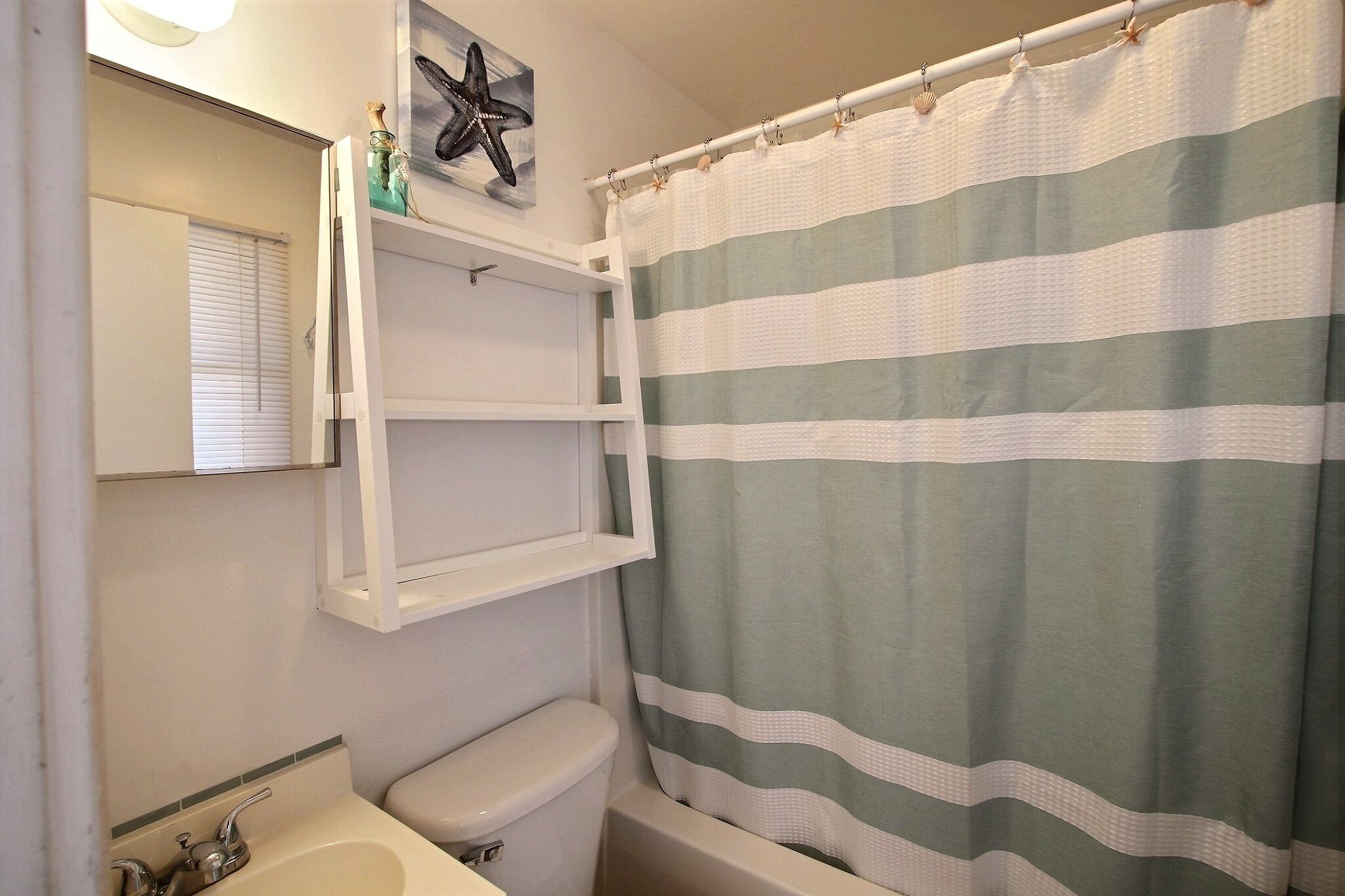 A bathroom with a striped shower curtain, a toilet, a sink, and a shelf with a starfish decoration.